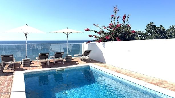Ein Poolbereich mit Liegestühlen und Sonnenschirmen, mit Blick auf einen klaren, blauen Himmel und den Ozean.