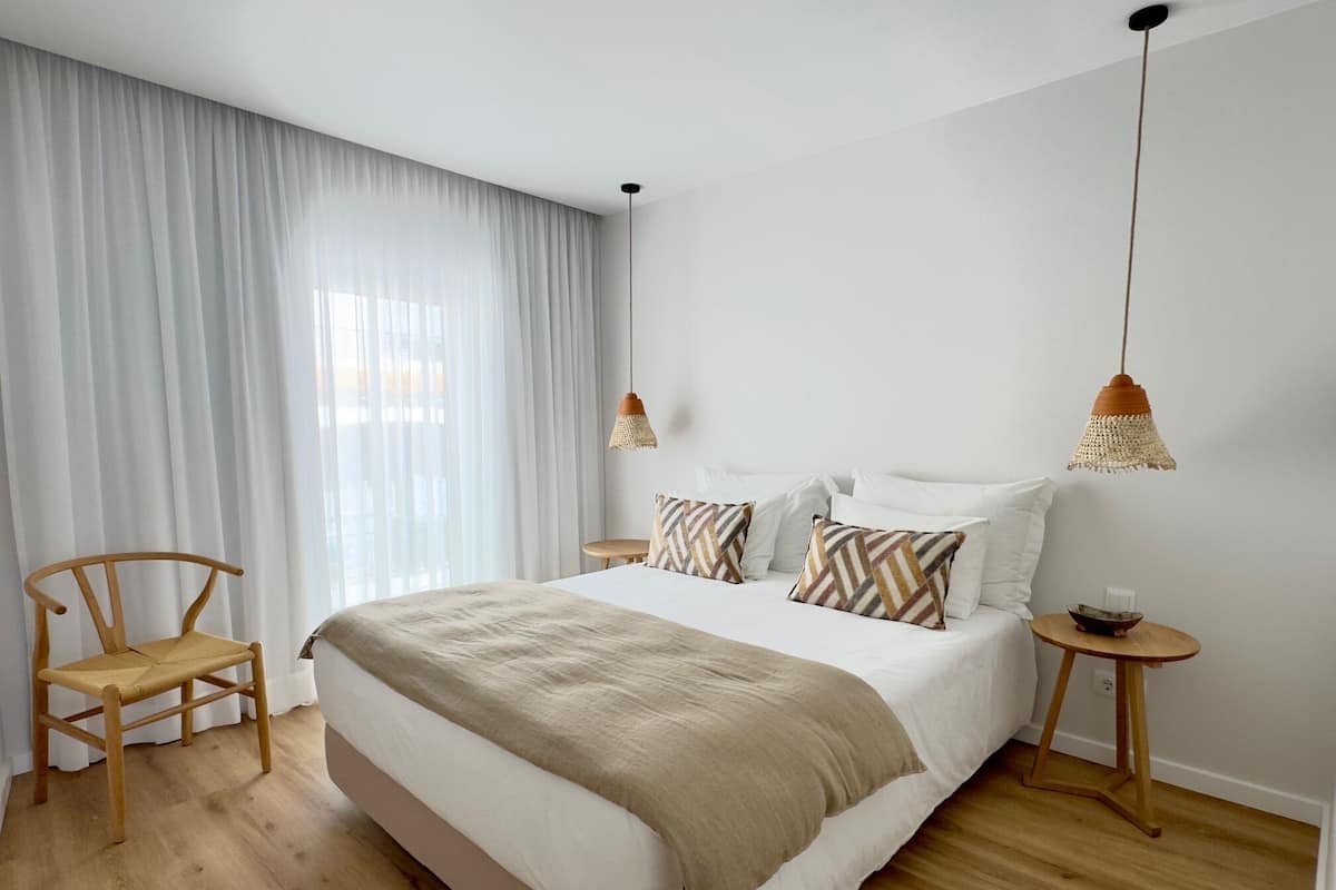 A bedroom with a large bed, two bedside tables, a chair, and a small table with a bowl.