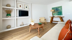 Ein modernes Wohnzimmer mit Holzboden, weißen Wänden, einer Couch, einem Couchtisch, einem Fernseher und einem Gemälde.