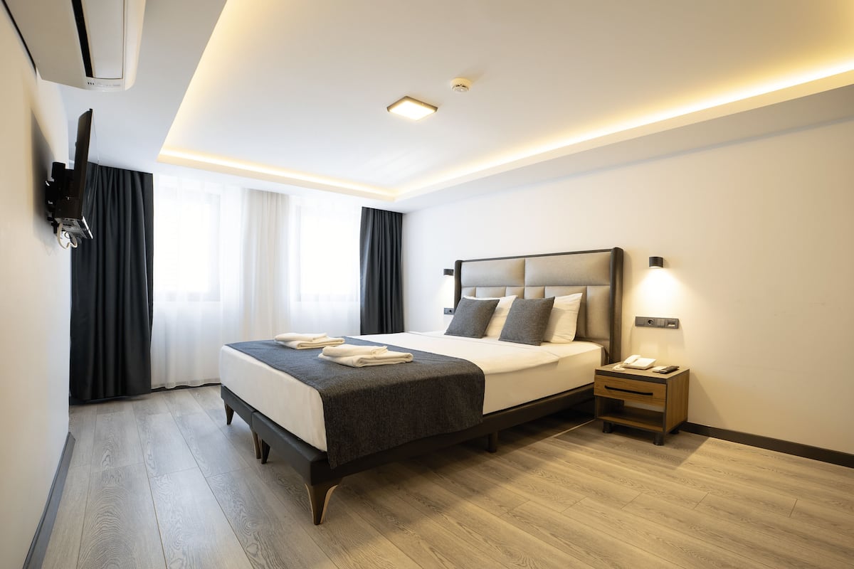 A modern hotel room with a large bed, bedside table, and a flat-screen TV mounted on the wall.