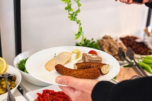 Una persona serve del cibo su un piatto, con diversi piatti e utensili visibili sullo sfondo.