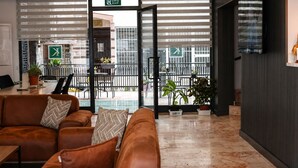 Un vestíbulo moderno con un sofá de cuero, un televisor montado en la pared y un vidrio que da a un área exterior con plantas y un balcón.