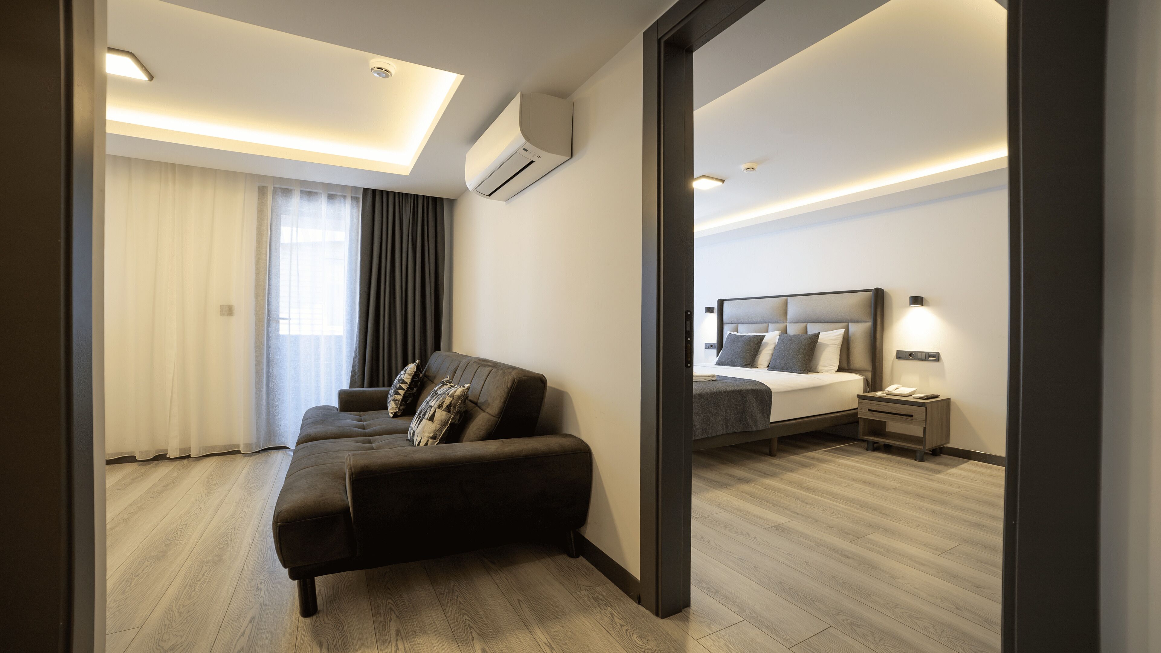 Una habitación de hotel moderna con sofá, cama, mesita de noche y espejo.