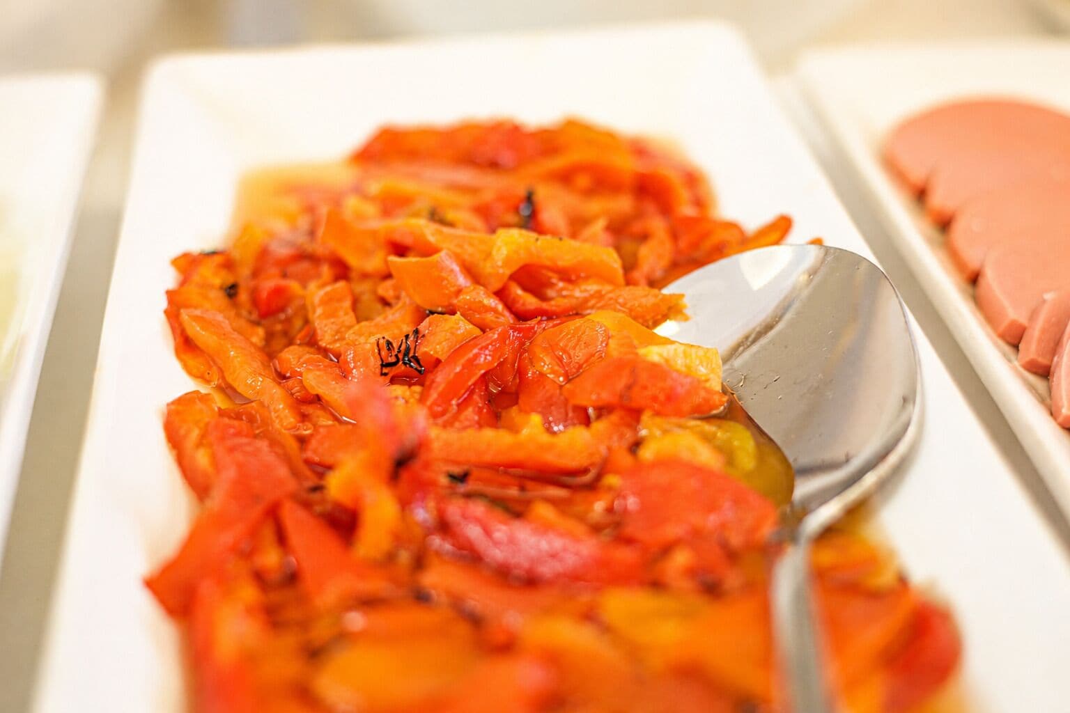 Primer plano de un plato con verduras en rodajas, posiblemente zanahorias, sobre un recipiente blanco y una cuchara.