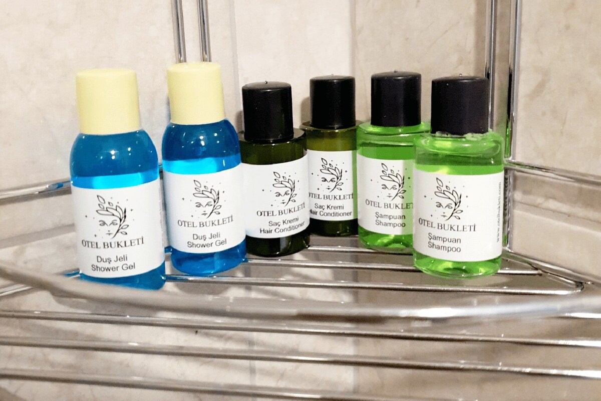 Un estante de baño con distintos artículos de aseo, incluyendo una botella azul de gel de ducha, una botella verde de champú y una botella negra de acondicionador para el cabello.