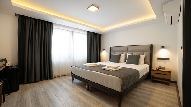 Una habitación de hotel moderna con una cama grande, lámparas de noche, un escritorio y una ventana con cortinas.