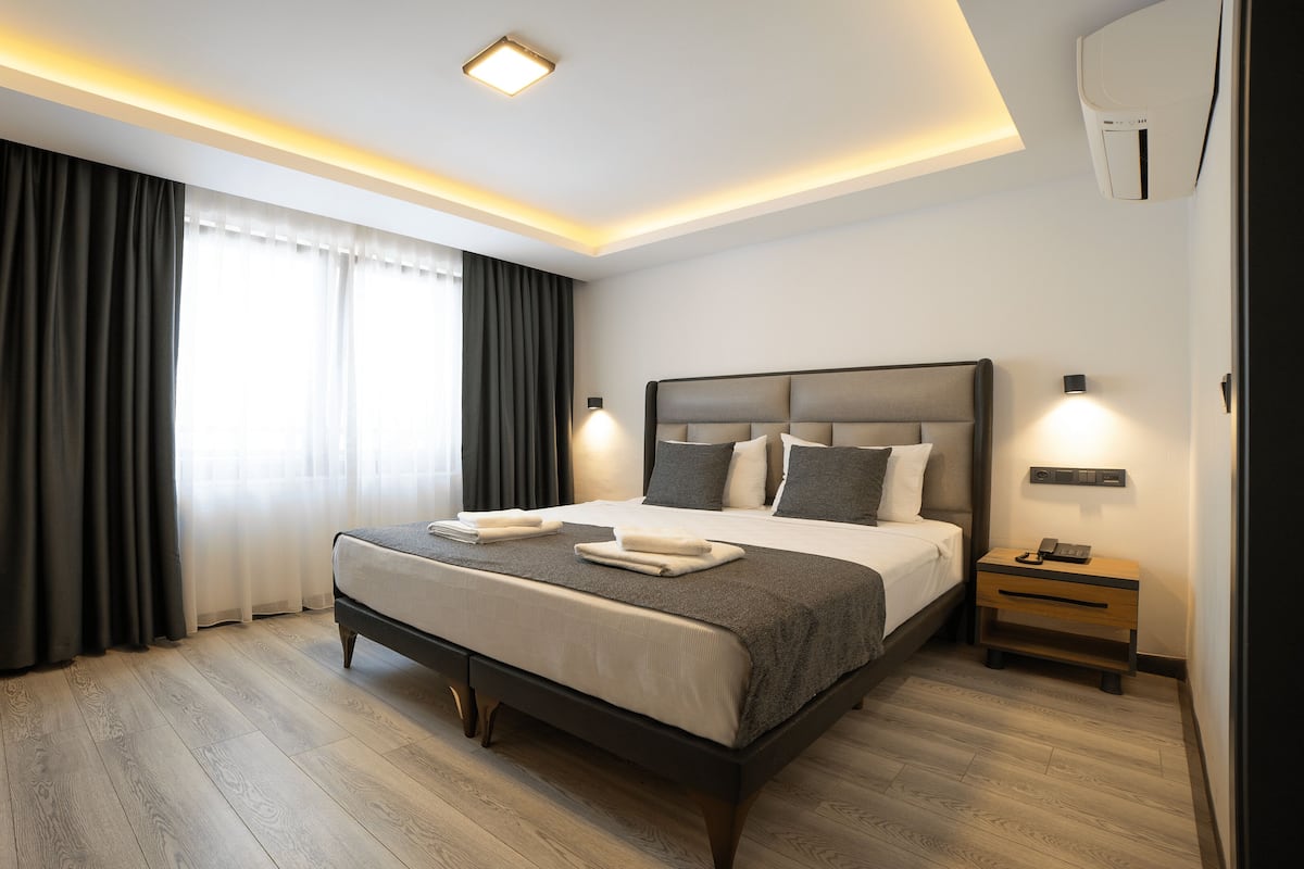 A modern hotel room with a large bed, bedside lamps, a desk, and a window with curtains.