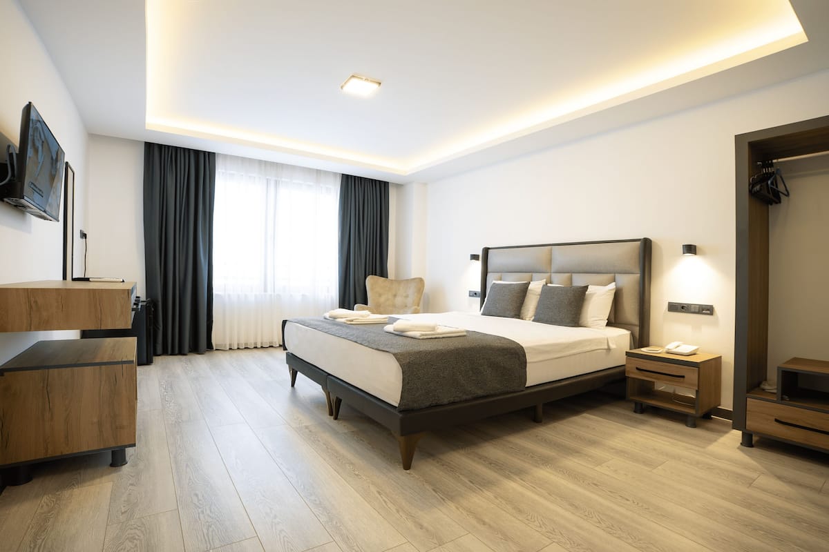 A modern hotel room with a large bed, bedside tables, a TV mounted on the wall, and a wardrobe.