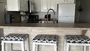 A kitchen with white cabinets, a stainless steel sink, and a built-in stove. There are three bar stools with patterned cushions. - Lakeview Luxury: Stunning 2 Bed, 2 Bath Condo with Breathtaking Lake Views (Camdenton)