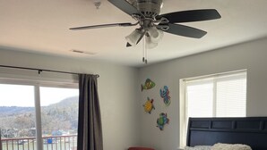 A bedroom with a bed, a ceiling fan, a window with blinds, a red chair, and a view of a body of water through a sliding door. - Lakeview Luxury: Stunning 2 Bed, 2 Bath Condo with Breathtaking Lake Views (Camdenton)