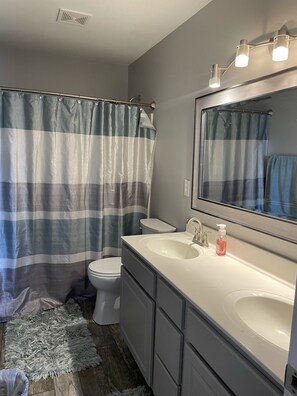 Un baño con cortina de ducha a rayas, un lavabo blanco, un espejo con luces y un inodoro.