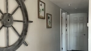 A hallway with a large wooden ship's wheel, two framed pictures, and a door at the end. - Lakeview Luxury: Stunning 2 Bed, 2 Bath Condo with Breathtaking Lake Views (Camdenton)