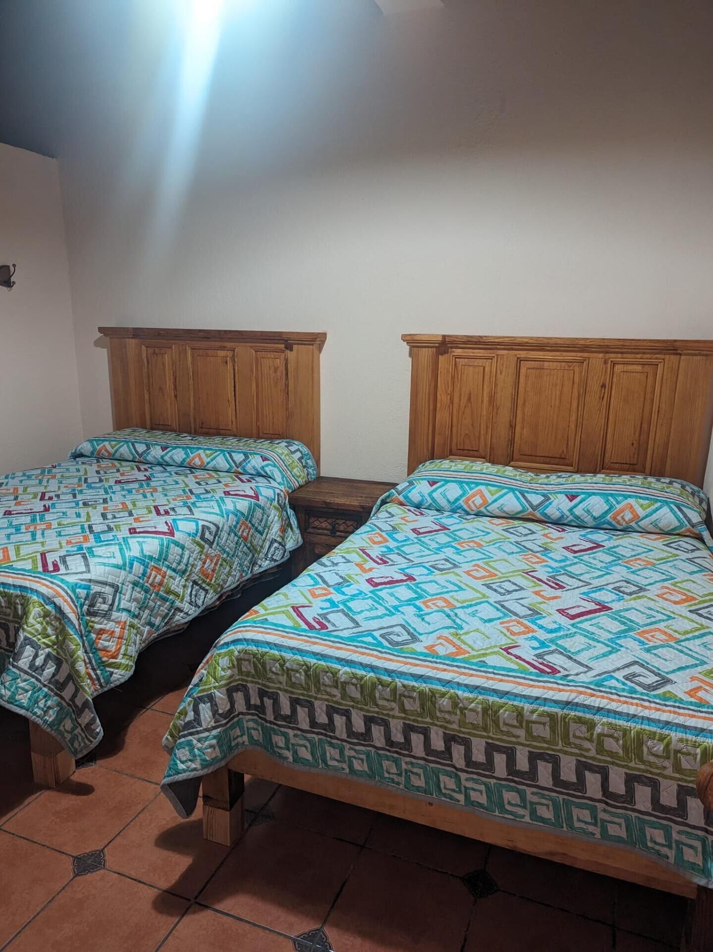 Two single beds with wooden headboards in a room with tiled flooring.