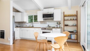 A modern kitchen with white cabinets, a microwave, a stove, and a dining area with wooden chairs. - Tranquil Treehouse - EV Charger (Cambria)