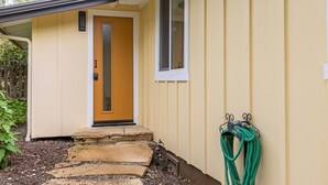 A yellow house with a front door, a window, and a garden hose on the right side. - Tranquil Treehouse - EV Charger (Cambria)