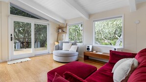A modern living room with a grey sofa, red cushions, a wooden coffee table, and a large window offering a view of trees. - Tranquil Treehouse - EV Charger (Cambria)