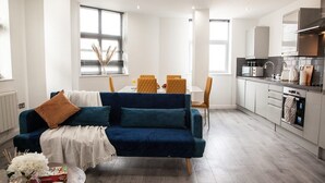 Una sala moderna con un sofá azul oscuro, una mesita de centro y un comedor con sillas amarillas.