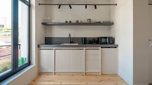 A modern kitchen with a large window, wooden flooring, white cabinets, and a black countertop. - Hoppersgr- Amazing apt in the heart of Athens - 3 (Athina)