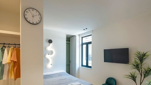 A modern bedroom with a bed, a wall-mounted TV, a wooden floor, and a plant. - Hoppersgr- Amazing apt in the heart of Athens - 3 (Athina)
