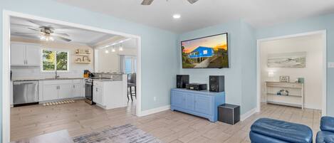 A spacious living area with a kitchen, a dining area, and a seating area with a blue ottoman.