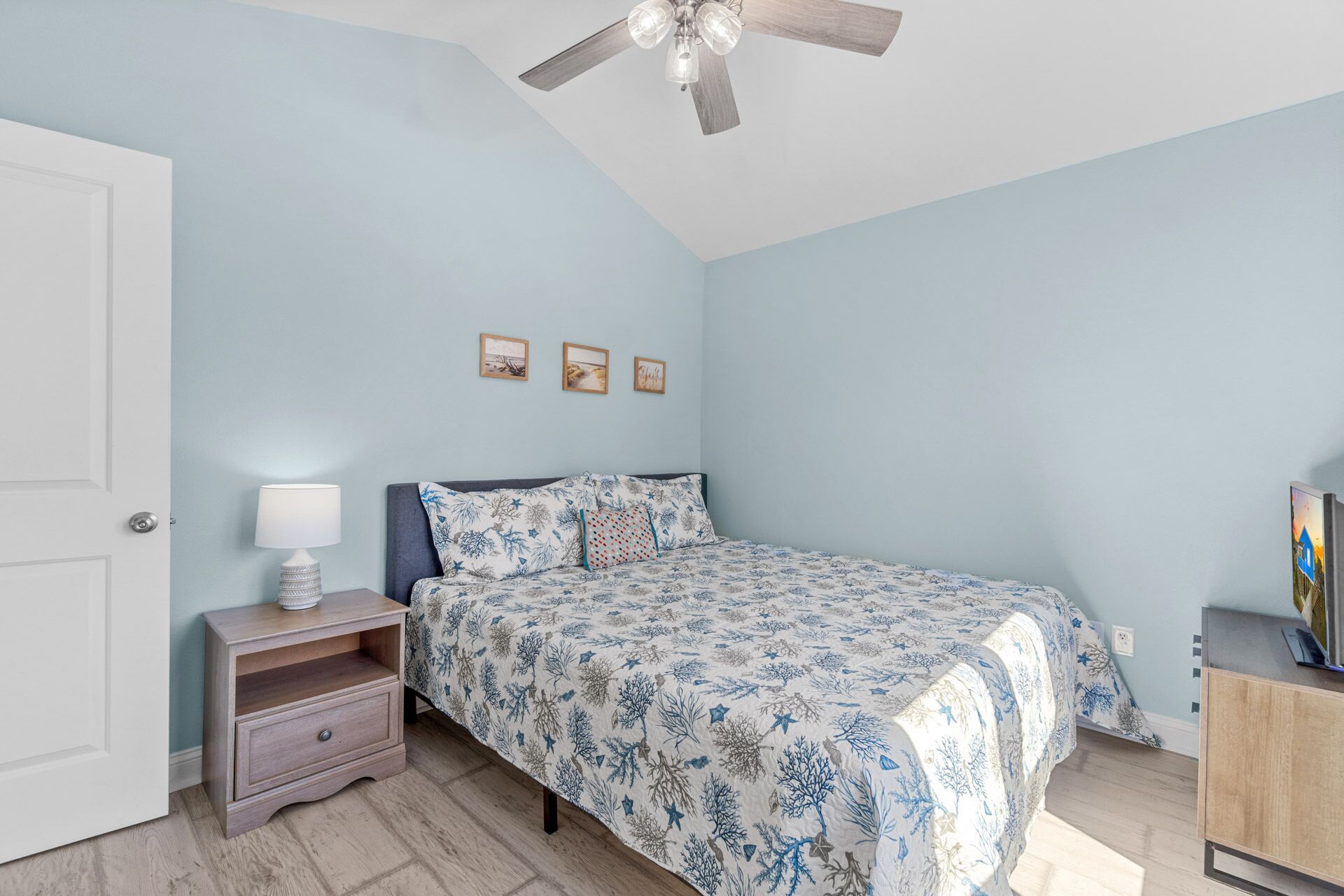 A bedroom with a bed, nightstand, lamp, ceiling fan, and wall art.