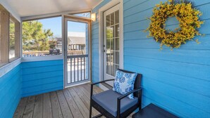Une véranda couverte à l’extérieur bleu, une chaise en osier avec un coussin et une guirlande jaune accrochée au mur.
