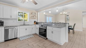 Une cuisine moderne avec des meubles blancs, un plan de travail en granit, des appareils électroménagers en acier inoxydable et un ventilateur de plafond.