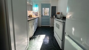 Een smalle keuken met witte kasten, een blauwe deur en een koelkast.