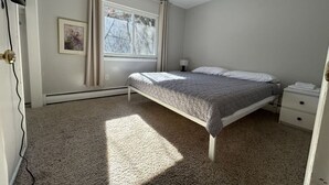 Ein Schlafzimmer mit Bett, Nachttisch, Lampe, Fenster und einem Bild an der Wand.