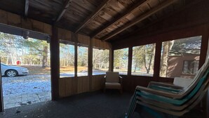 A covered outdoor seating area with a bench and a chair, a car parked outside, and a view of trees and a building. - 2 BR, walk to beach, volleyball (Sanilac Township)