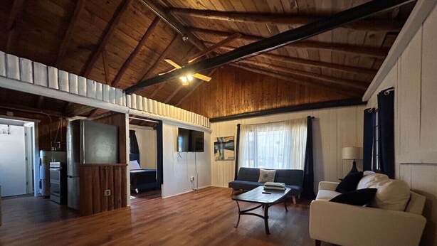 A spacious living area with wooden flooring, a white sofa, a coffee table, and a television mounted on the wall. - 2 BR, walk to beach, volleyball (Sanilac Township)