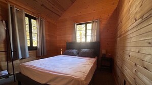 Une chambre à coucher dans une cabane en bois, avec un lit, deux fenêtres et une table de chevet.