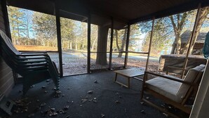 Un espace extérieur aménagé, abrité et doté de bancs et de chaises, entouré d’arbres et offrant une vue sur une zone boisée.