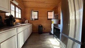 Une cuisine compacte avec des murs en bois, un réfrigérateur en acier inoxydable et une petite poubelle.