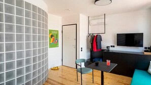 A modern living room with a curved wall, a dining area with a table and chairs, a kitchen area with a TV, and a sofa. - Hoppersgr- Amazing apt in the heart of Athens - 4 (Athina)