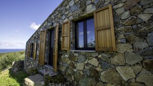 Un bâtiment en pierre avec des volets en bois, un escalier en pierre et une vue sur la mer.