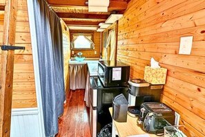 A narrow wooden cabin interior with a kitchenette area, including a stove, microwave, and various appliances. - 2  Lakefront, Comfortable Bed, Great Fishing (Eastland)