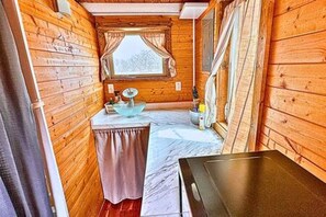 A narrow wooden cabin interior with a window, a sink, and a table.