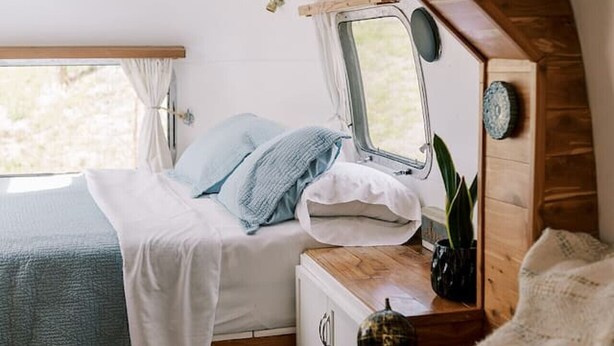 Un dormitorio acogedor en una autocaravana, con cama, un escritorio pequeño, un espejo y una ventana.