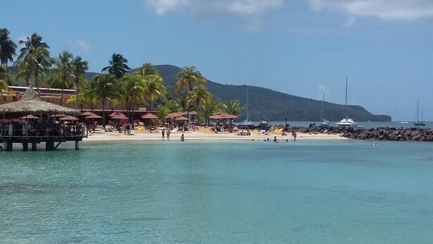 Une plage bordée de palmiers, une structure à toit de chaume et des bateaux sur l’eau.