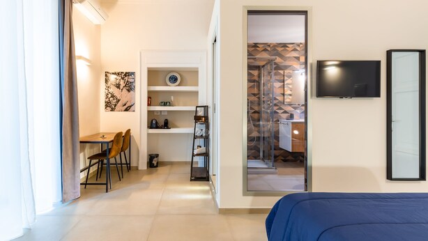 A modern hotel room with a bed, a desk with chairs, a TV, and a bathroom visible through an open door. - Residenza Partanna by Napoliapartments (Naples)