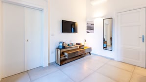 A hallway with a white tiled floor, a wooden console table with drawers, a flat-screen TV mounted on the wall, a mirror, and a door on the right. - Residenza Partanna by Napoliapartments (Naples)