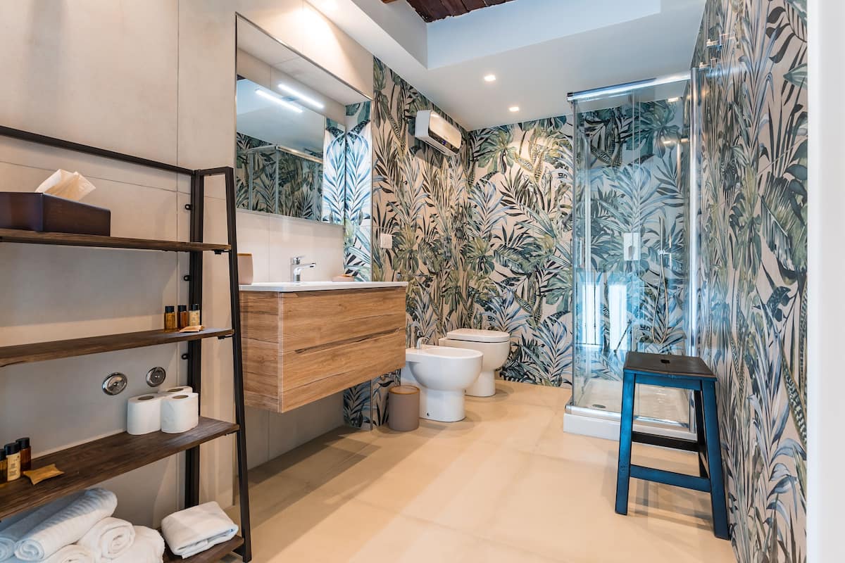 Ein modernes Badezimmer mit einem Holzwaschtisch, zwei Toiletten, einer Duschkabine mit Glastüren und einem blauen Hocker.