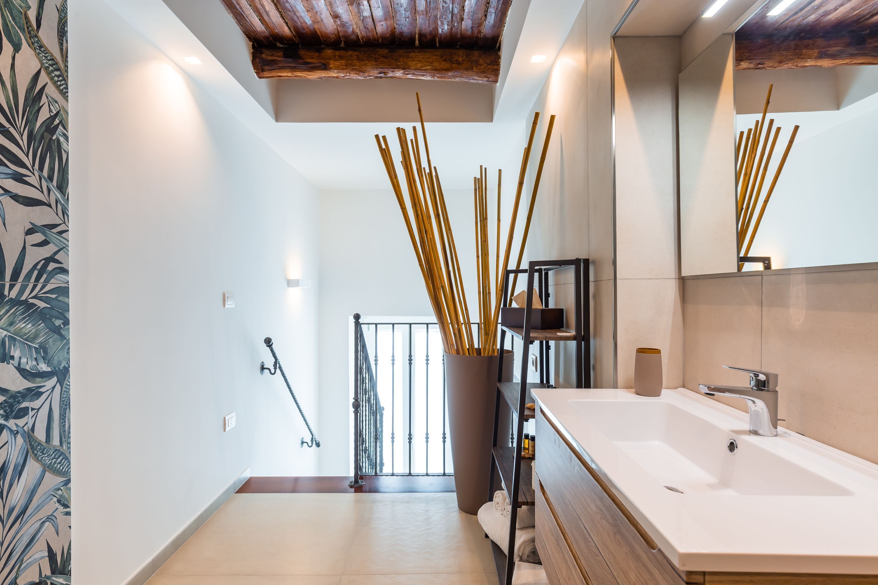 A modern bathroom with a large mirror, white sink, and a wooden ceiling.