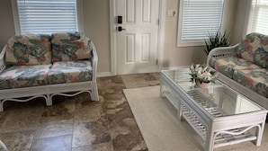 A living room with a white door, two sofas with floral upholstery, a glass coffee table, and a patterned rug.