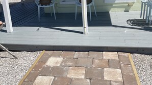 A covered porch with a wooden deck, two windows with blinds, and two wicker chairs.