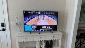 A television on a white console with drawers, displaying a basketball game.