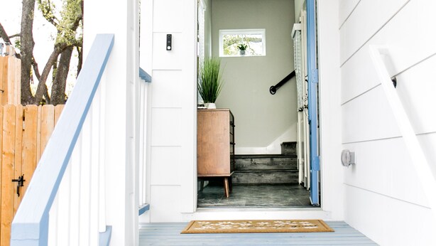 A narrow, white-walled hallway with a blue door leading to a room. A wooden cabinet and a potted plant are visible in the room. - Mid-Century Modern Home is 10 minutes from Downtown Houston (Houston)