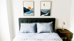A bedroom with a bed, two pillows, a nightstand, a lamp, and two framed artworks on the wall. - Mid-Century Modern Home is 10 minutes from Downtown Houston (Houston)