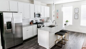 A modern kitchen with white cabinets, stainless steel appliances, and a central island with stools. - Mid-Century Modern Home is 10 minutes from Downtown Houston (Houston)
